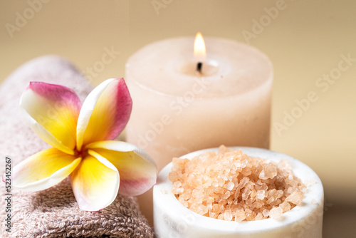 Beautiful SPA composition , burning candle, towel with frangipani flowe and salt scrub on beige background . Beauty and wellness centre concept . Close up