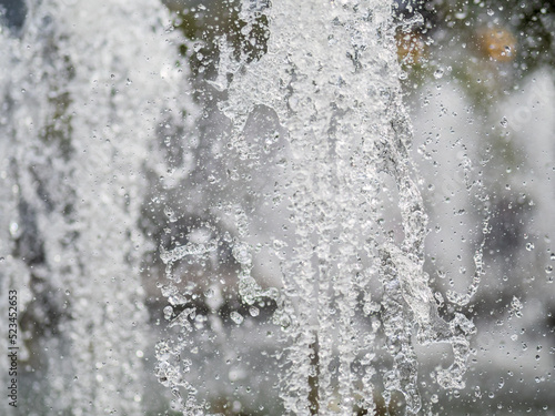 Splashes of water on dark background. Water sprays in sunny day close-up.