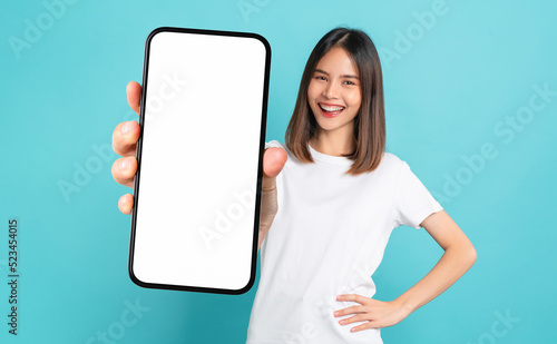 Studio shot of Beautiful Asian woman holding smartphone mockup of blank screen and smiling on blue background. © sitthiphong