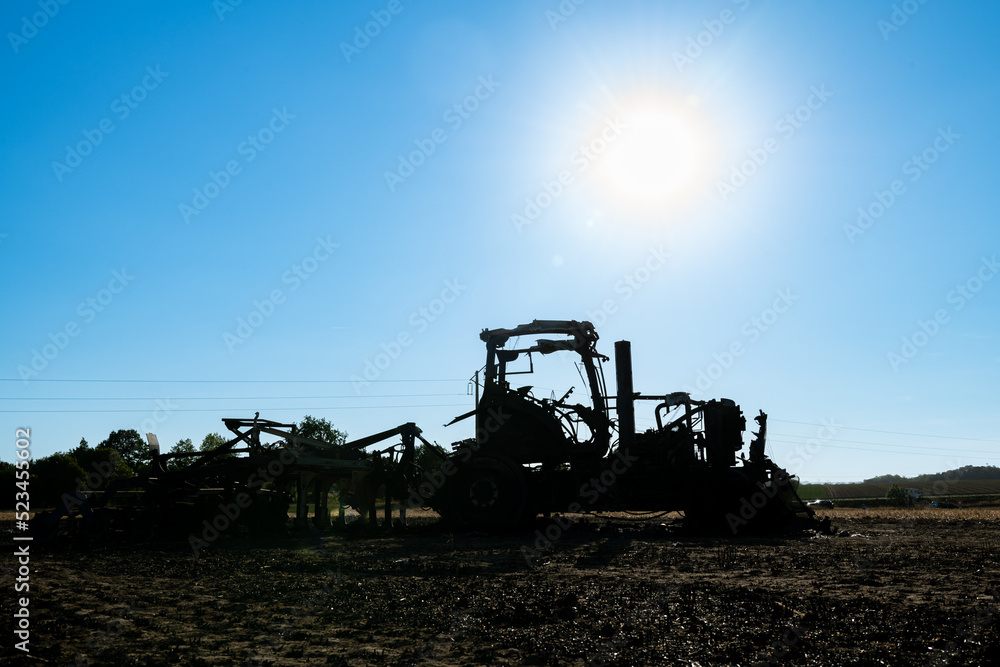 Fototapeta premium Carcasse de tracteur calciné suite à un incendie dans le champ de chaume lors de forte canicule