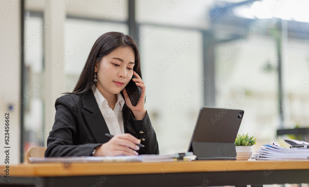 Business Asian woman talking on the phone and working with laptop calculator document on an office desk, planning analyzing the financial report, business plan investment, finance analysis concept. Business Asian woman talking on the phone and working with laptop calculator document on an office desk, planning analyzing the financial report, business plan investment, finance analysis concept.