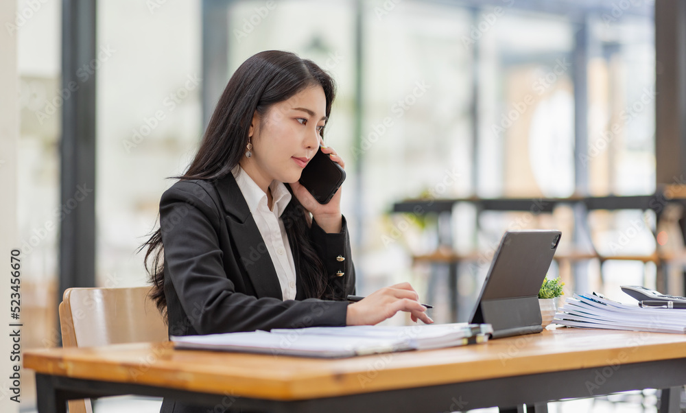 Business Asian woman talking on the phone and working with laptop calculator document on an office desk, planning analyzing the financial report, business plan investment, finance analysis concept. Business Asian woman talking on the phone and working with laptop calculator document on an office desk, planning analyzing the financial report, business plan investment, finance analysis concept.