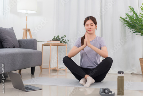 Yoga exercise concept, Young Asian woman in lotus position while doing yoga exercise online at home