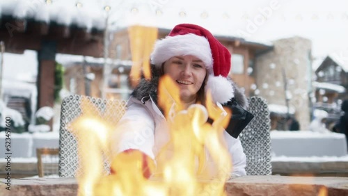 Woman in red Christmas hat roasting marshmallows in fire pit having after ski fun leisure activity at Winter holiday ski resort in Apsen. POV video of young woman grilling marshmallow stick in bonfire photo