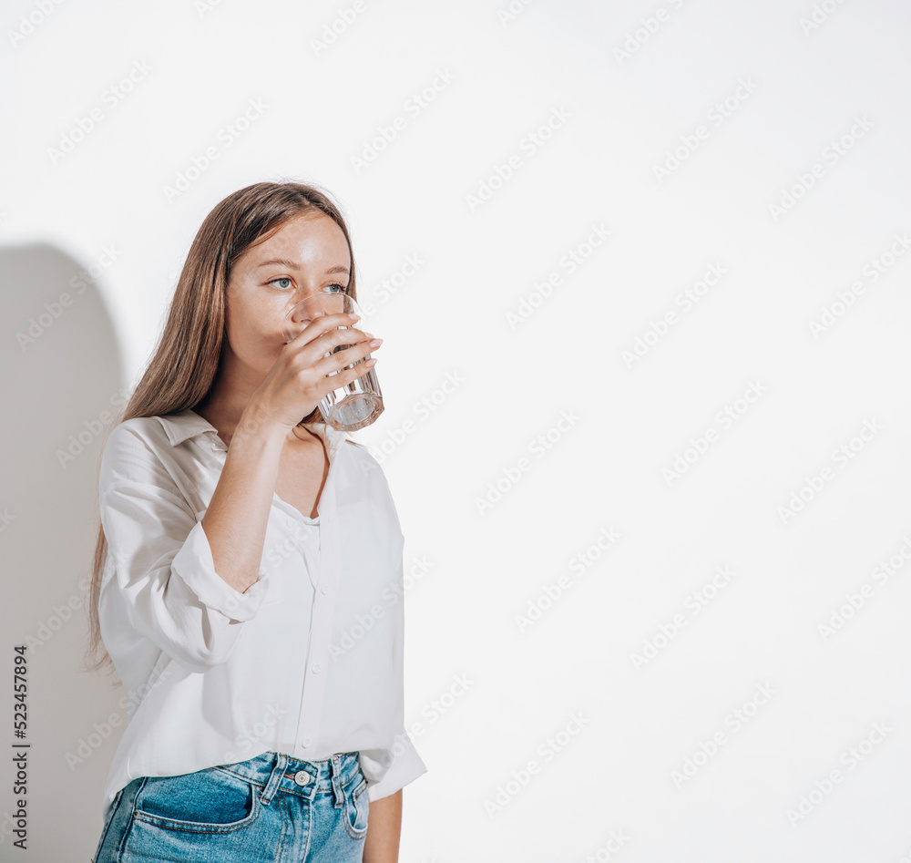 Girl drinks water from a glass cup on a white background. The concept of maintaining water balance Girl drinks water from a glass cup on a white background. The concept of maintaining water balance
