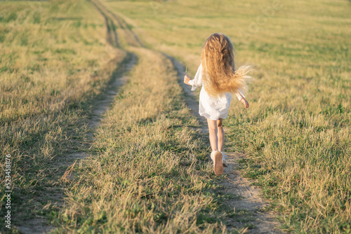 Happy childhood in the village. A child with long blonde hair runs across the field. Joyful children's games. Summer in the village at grandma's