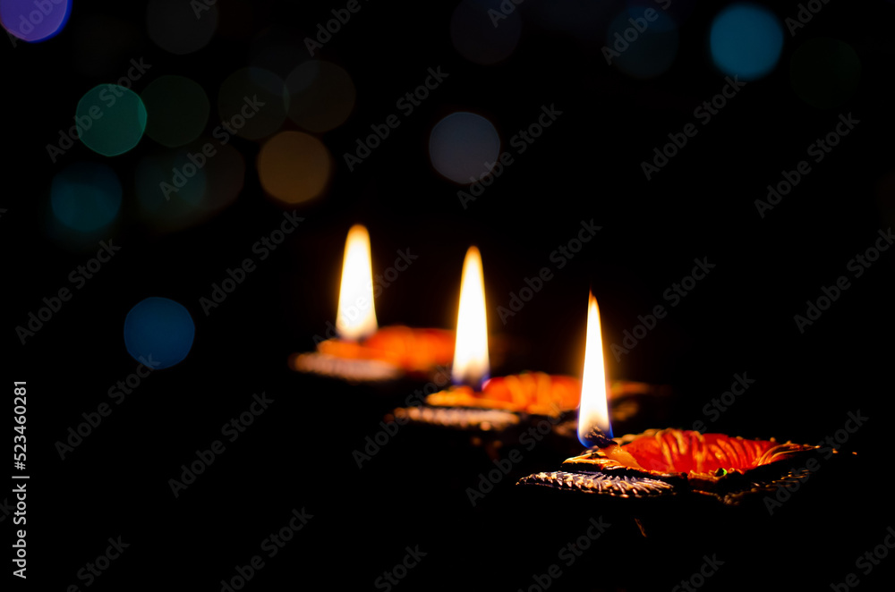 Selective focus on flame of clay diya lamps lit on dark background with colorful bokeh lights. Diwali festival concept.