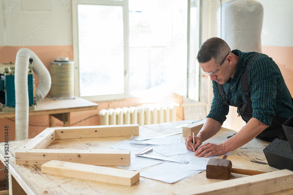 A portrait of a carpenter in goggles and work overalls draws a blueprint for a workshop. A portrait of a carpenter in goggles and work overalls draws a blueprint for a workshop.