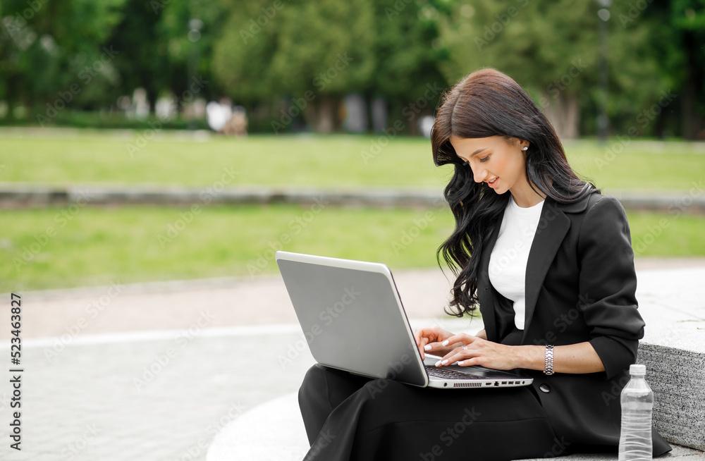 Attractive stylish woman working on laptop, freelancer sitting in the park on the stairs Attractive stylish woman working on laptop, freelancer sitting in the park on the stairs