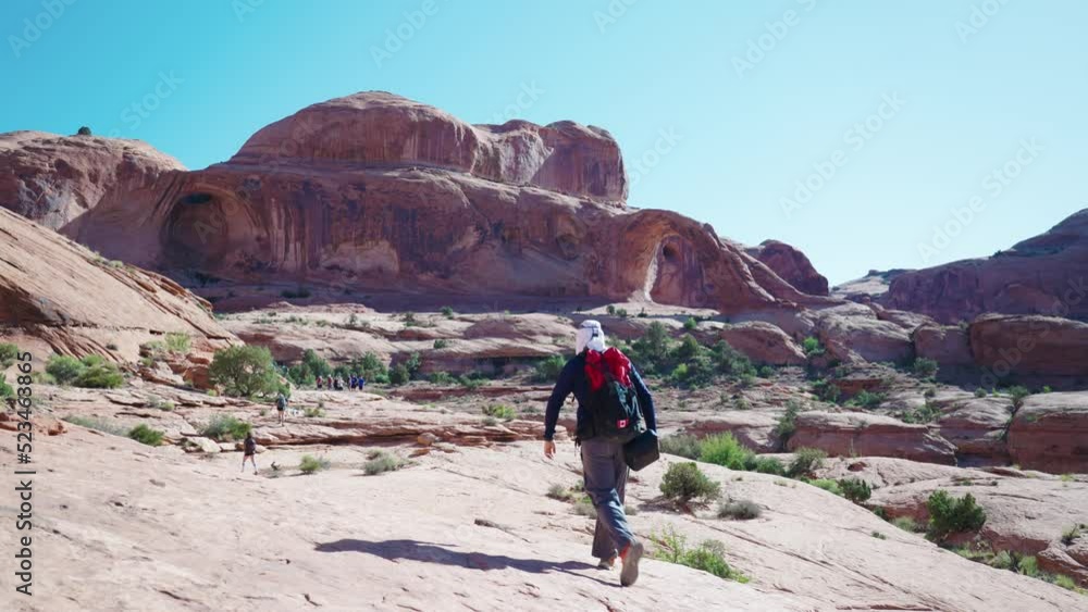Hiker walking with Corona Arch in the distance - Moab, United States Hiker walking with Corona Arch in the distance - Moab, United States