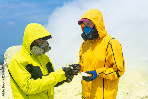 volcanologists on the slope of the volcano examines samples of minerals against the backdrop of smoking sulfur fumaroles
