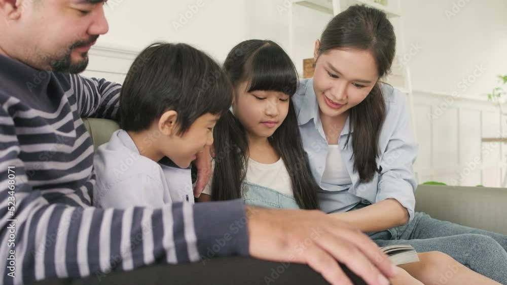 Asian Thai family, adult dad, mum, and children happiness home living relaxing activities and reading book together, leisure on sofa in white room house, lovely weekend, wellbeing domestic lifestyle. Asian Thai family, adult dad, mum, and children happiness home living relaxing activities and reading book together, leisure on sofa in white room house, lovely weekend, wellbeing domestic lifestyle.
