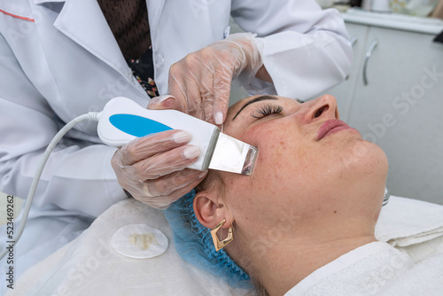 cosmetologist performs a cavitation procedure on the client's face in the salon.