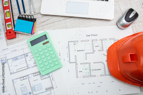 People working with construction drawings and tools at a wooden table.