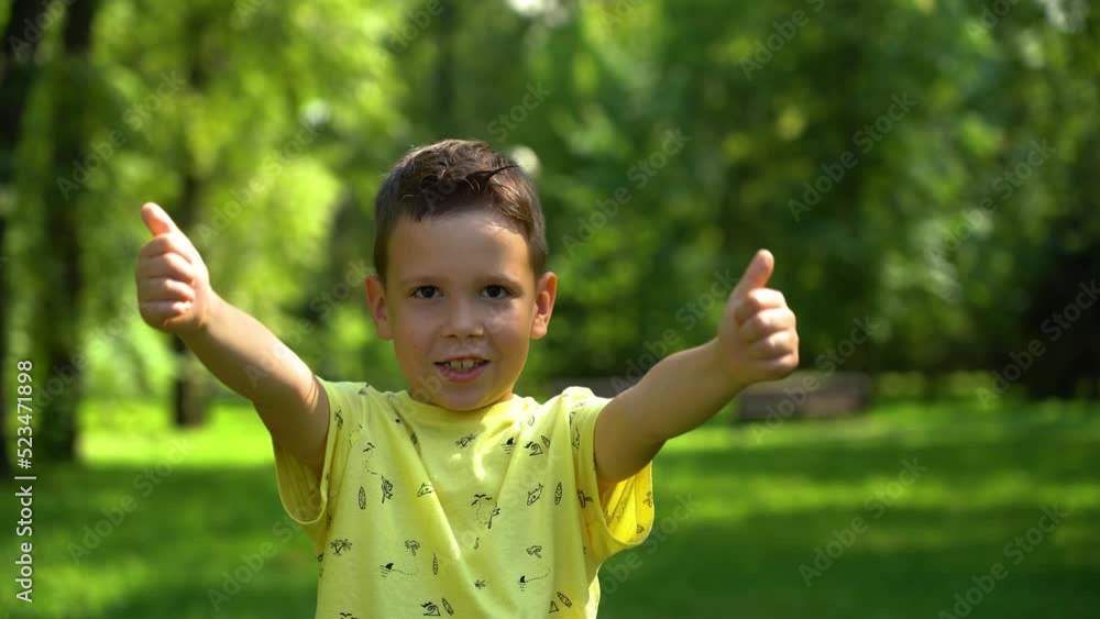 Caucasian boy showing class gestures on a sunny summer day in a green park under the trees. The boy shows gestures with his fingers cool in the park among the green trees in the background Caucasian boy showing class gestures on a sunny summer day in a green park under the trees. The boy shows gestures with his fingers cool in the park among the green trees in the background