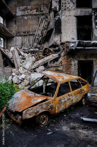 Burned car after the terror attacks a result of the Russian invasion of Ukraine the backdrop of a war-torn house. Exploded car. Damage auto of civilians. War in Ukraine. War crimes.