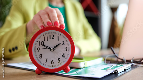 Woman putting red alarm clock on desk, time management and deadline