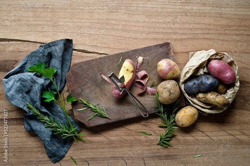 Herbs, dish towel, cutting board, potato peeler and different varieties of raw potatoes photo