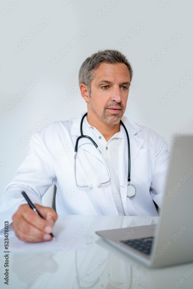 Mature doctor using laptop at desk in medical practice