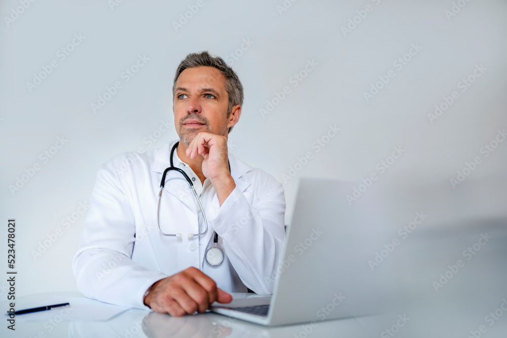 Pensive mature doctor sitting at desk in medical practice Pensive mature doctor sitting at desk in medical practice