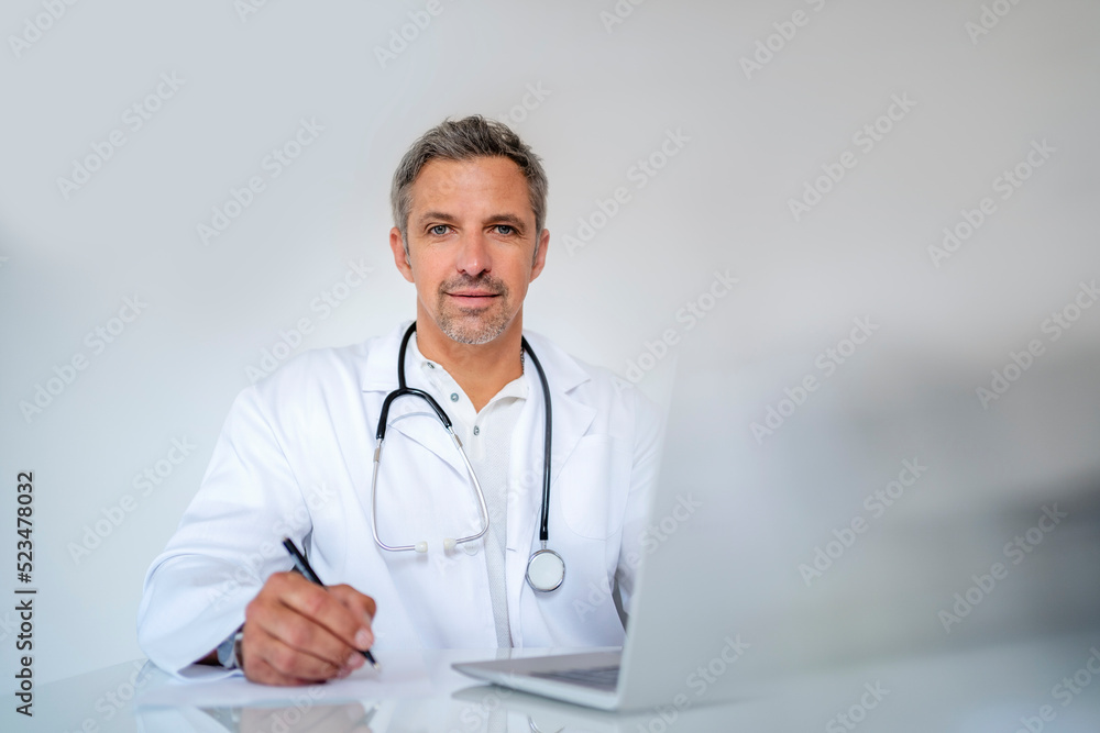 Portrait of mature doctor sitting at desk in medical practice Portrait of mature doctor sitting at desk in medical practice
