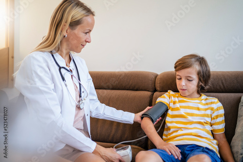 Female doctor taking boy's blood pressure on couch at home photo
