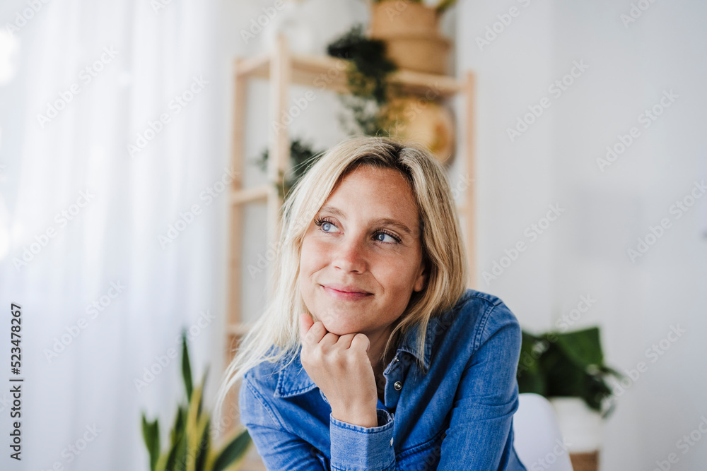 Blond woman with hand on chin day dreaming at home Blond woman with hand on chin day dreaming at home