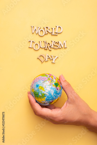 World Tourism Day text from wooden letters on a yellow color background with globe in female hands top view photo