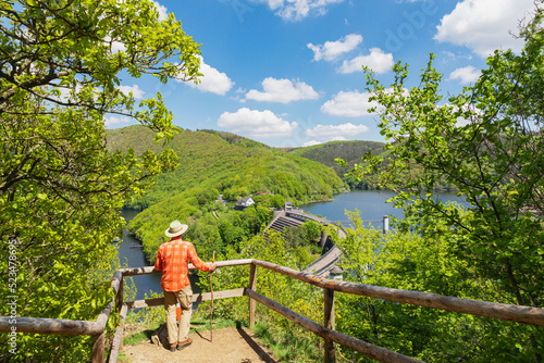 Senior man standing with walking cane by railing looking at Urft Dam, Eifel National Park, Germany photo