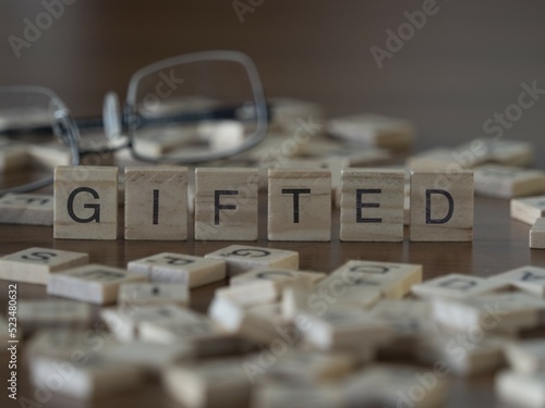 Gifted word or concept represented by wooden letter tiles on a wooden table with glasses and a book