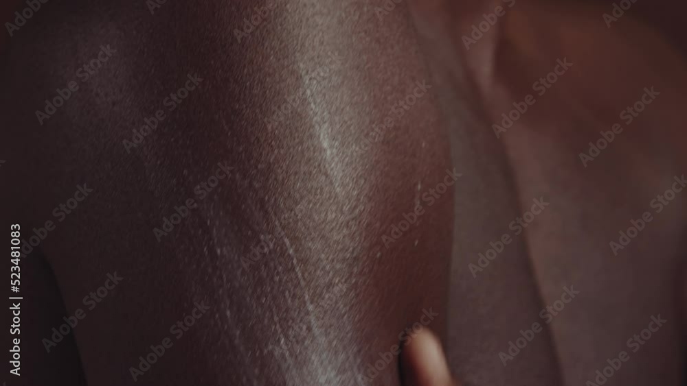 Close-up slowmo of unrecognizable young African American man spreading nourishing cream over his shoulder and chest, brown background Close-up slowmo of unrecognizable young African American man spreading nourishing cream over his shoulder and chest, brown background