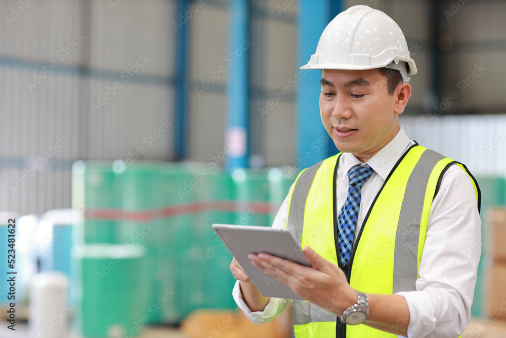 Architect or engineering man and worker standing and checking large warehouse with tablet. Asian business manager looking in future with warehouse building background. Architect or engineering man and worker standing and checking large warehouse with tablet. Asian business manager looking in future with warehouse building background.