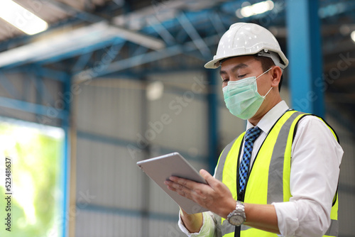 Architect or engineering man and worker standing and checking large warehouse with tablet. Asian business manager looking in future with warehouse building background.