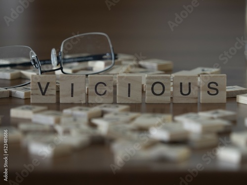 Vicious word or concept represented by wooden letter tiles on a wooden table with glasses and a book photo