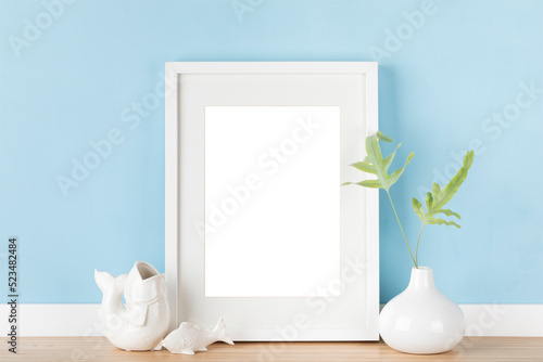 Elegant vertical white transparent picture frame with matte poster mockup and Japanese decoration in front of pastel blue wall.