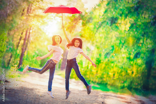 Two funny girls with a red umbrella for a walk in the summer forest. Bright sunny day