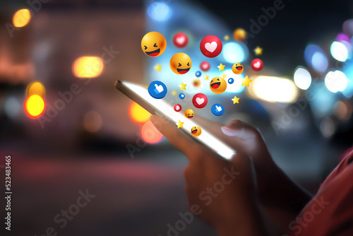 Woman using smartphone at night and social 3D graphics icon on screen with beautiful bokeh. girl's hand using a smartphone social icons on smartphone screen