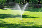 Irrigation system watering green grass, blurred background.