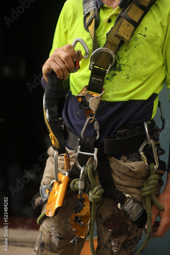 Rope access inspector clipping locking Karabiner into front of full body safety abseiling harness loop with self controlled stop a fall descent safety device absorbing lanyard attached at the end 