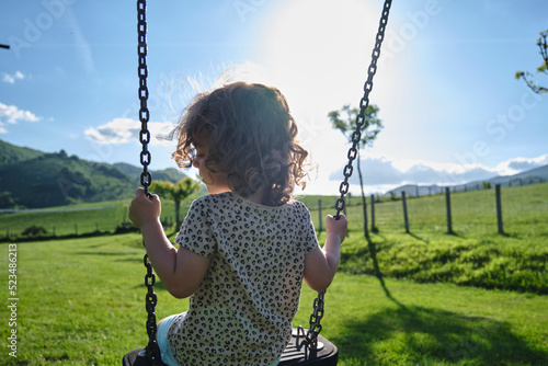 little caucasian girl alone and sad on the swing in the park - playground- concept of shyness, autism, social problems photo