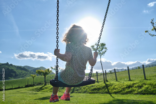 little caucasian girl alone and sad on the swing in the park - playground- concept of shyness, autism, social problems