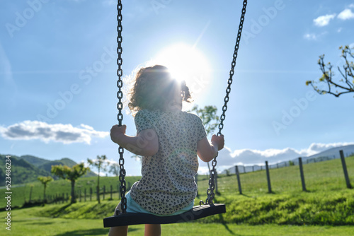 little caucasian girl alone and sad on the swing in the park - playground- concept of shyness, autism, social problems