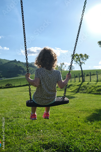 little caucasian girl alone and sad on the swing in the park - playground- concept of shyness, autism, social problems