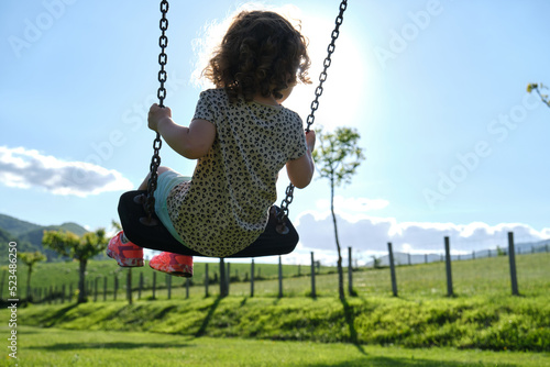 little caucasian girl alone and sad on the swing in the park - playground- concept of shyness, autism, social problems