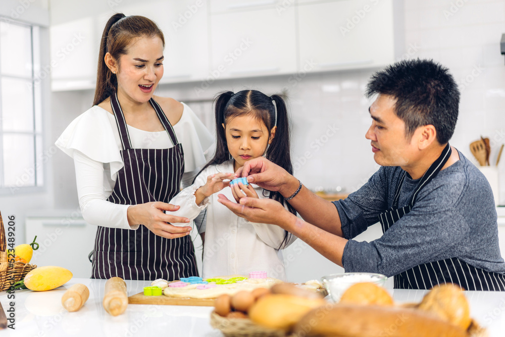 Portrait of enjoy happy love asian family father and mother with little asian girl daughter child play and having fun cooking food together with baking cookie and cake ingredient in kitchen