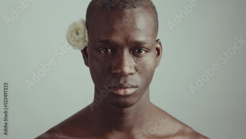 Minimalistic studio portrait of handsome young adult Black man with rose behind his ear raising his head looking at camera photo