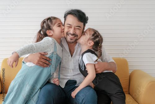 Two daughters kiss their father's cheek and hug her father.