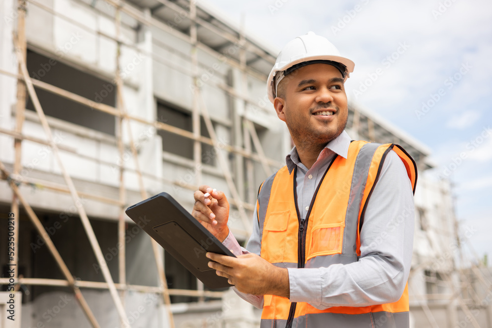 Confident asian engineer man Using tablet for checking and maintenance to inspection at modern home building construction. Architect working with white safety helmet in construction site