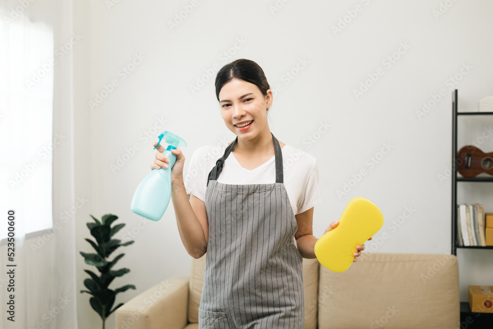 Young beautiful woman with apron and rubber glove ready for cleaning home background. Housekeeping housework or maid worker holding spray bottle and sponge Young beautiful woman with apron and rubber glove ready for cleaning home background. Housekeeping housework or maid worker holding spray bottle and sponge
