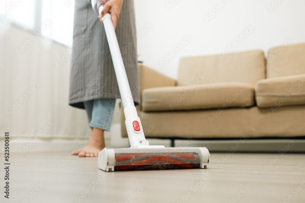 Close up housewife using vacuum cleaner on the floor. Wearing an apron to clean the living room at house. Young woman is happy to clean home. Maid cleaning service. Close up housewife using vacuum cleaner on the floor. Wearing an apron to clean the living room at house. Young woman is happy to clean home. Maid cleaning service.